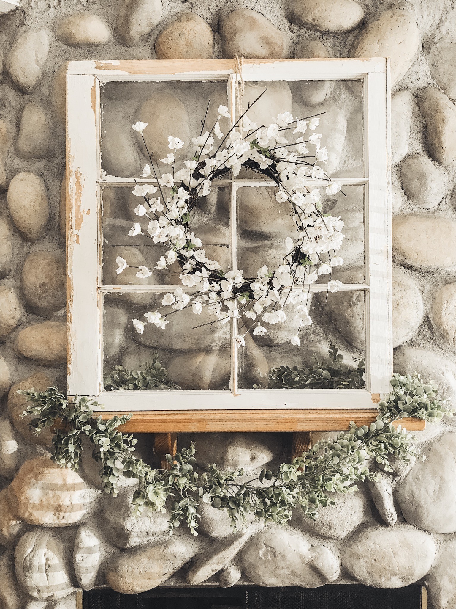 Farmhouse mantle. White old window with a wreath hanging on it and garland wrapping around the ledge.