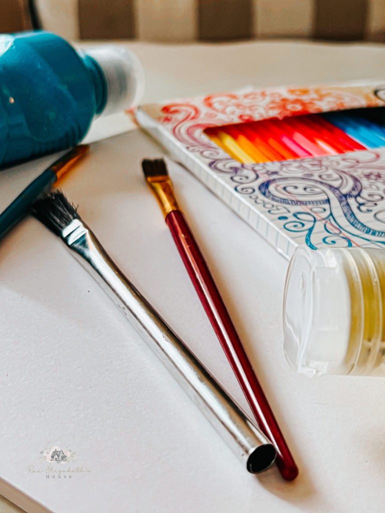 Paintbrushes, colored pencils, and paint sitting on paper