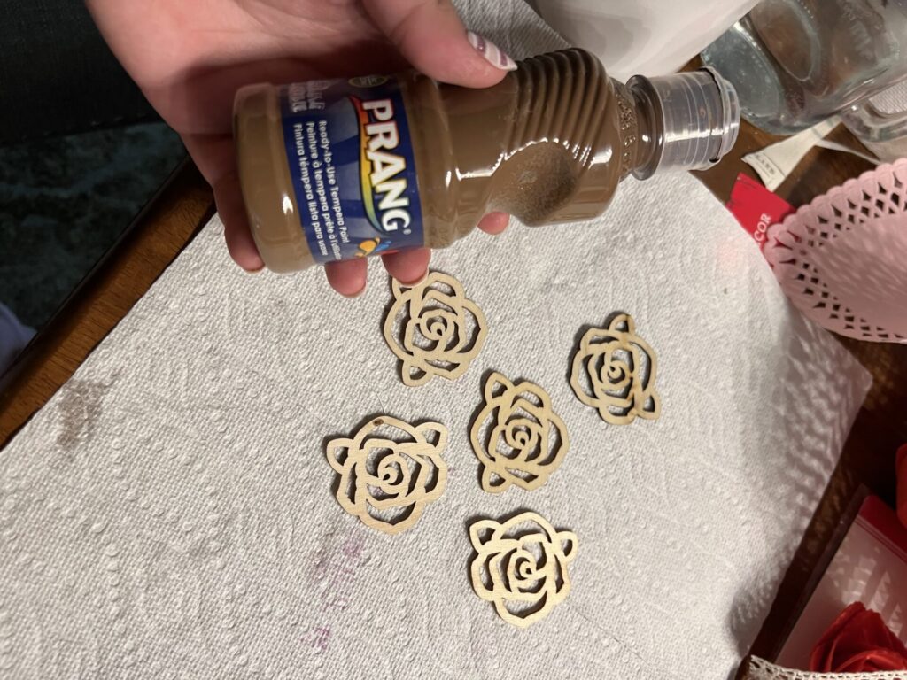showing a bottle of brown paint next to the plain wood rose appliqués