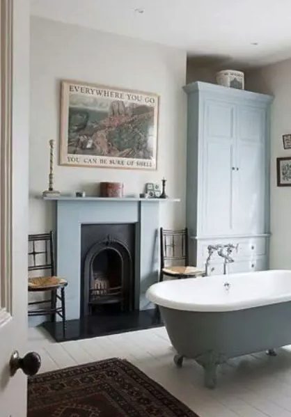 beautiful blue vintage bathroom with a free standing tub, a fireplace and a rug.