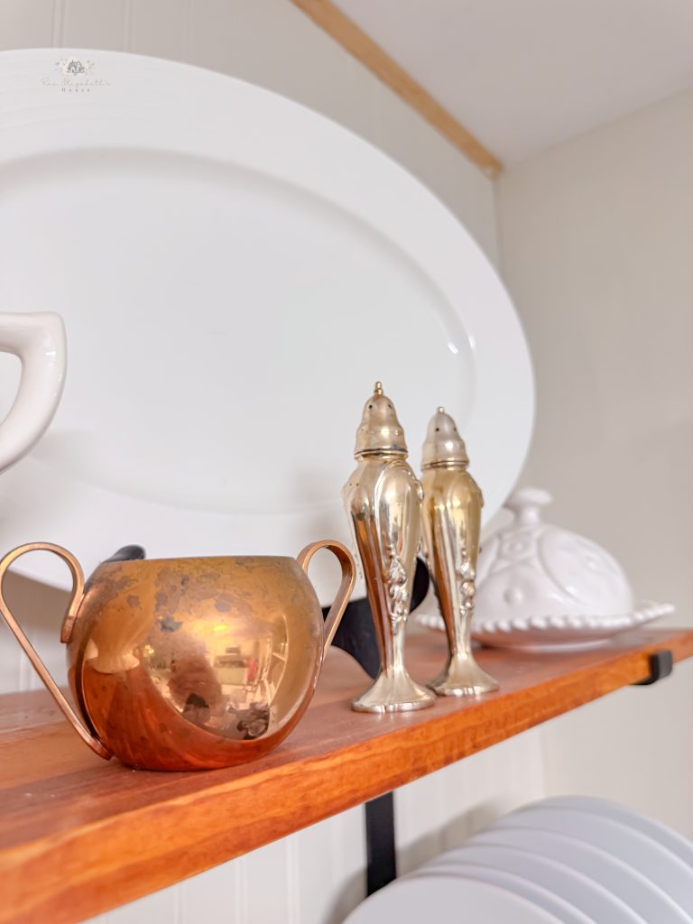 Up close shot of silver salt and pepper shakers and copper cup on an open shelf